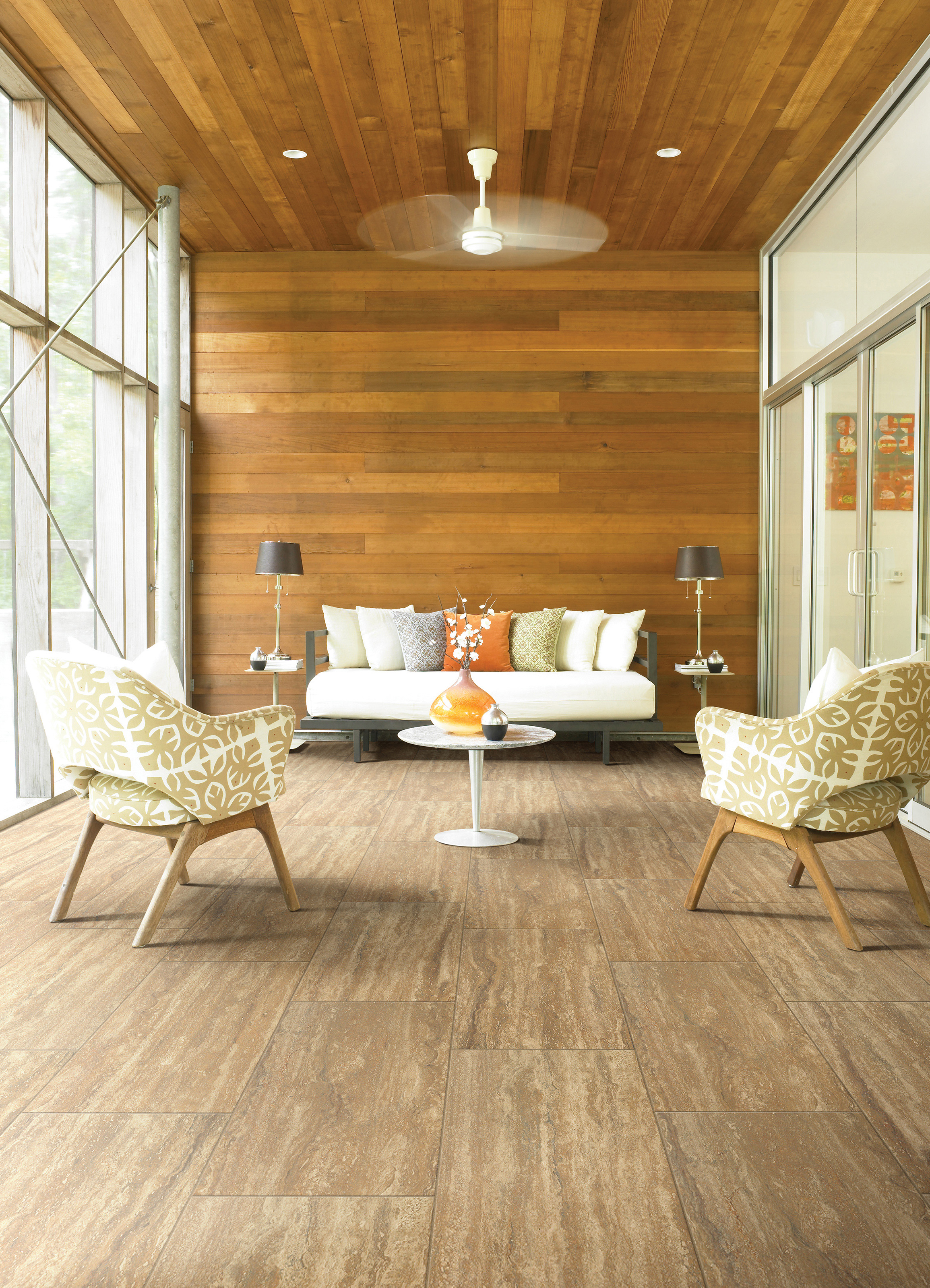 Sophia Dorado wood-look tile in porch setting. White arm chairs, couch, small table, and wooded walls present.